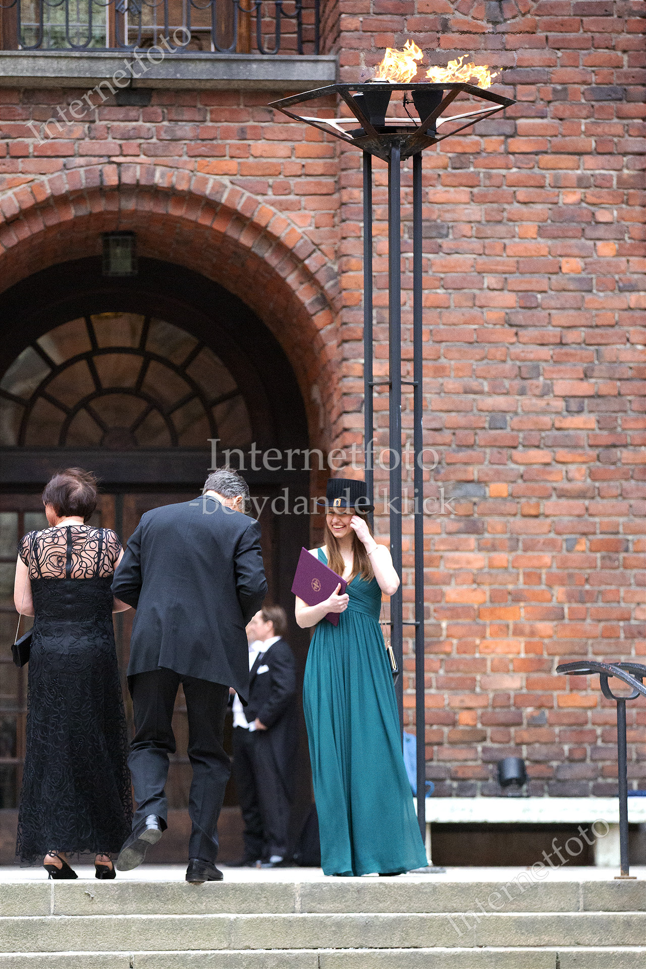 Ny KI-doktor i aftonklänning, doktorshatt och diplom står under brinnande eld utanför Stockholms stadshus.