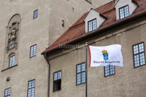Sveriges Domstolars vita flagga med emblem blå botten, gult svärd och våg med vågskålar samt texten Sveriges Domstolar. Flaggan är hissad på en svart flaggstång vid Stockholms tingsrätt på Scheelegatan 7 i Stockholm. Byggnaden har en putsad fasad i beige ton, röda tegeltak, takkupor och fönster med spröjs. På tornets fasad syns även en dekorativ steninramning med kung St Erik som håller i ett svärd. Under finns text: Lag och rätt 1914.